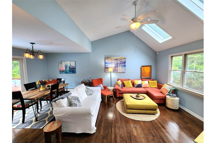 Living area featuring ceiling fan, wood finished floors, a chandelier, a skylight, and lofted ceiling