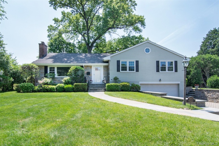 View of front of property featuring a chimney, an attached garage, a front lawn, and stone siding