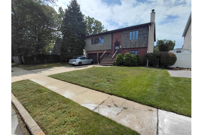 Bi-level home featuring an attached garage, brick siding, concrete driveway, a chimney, and a front lawn