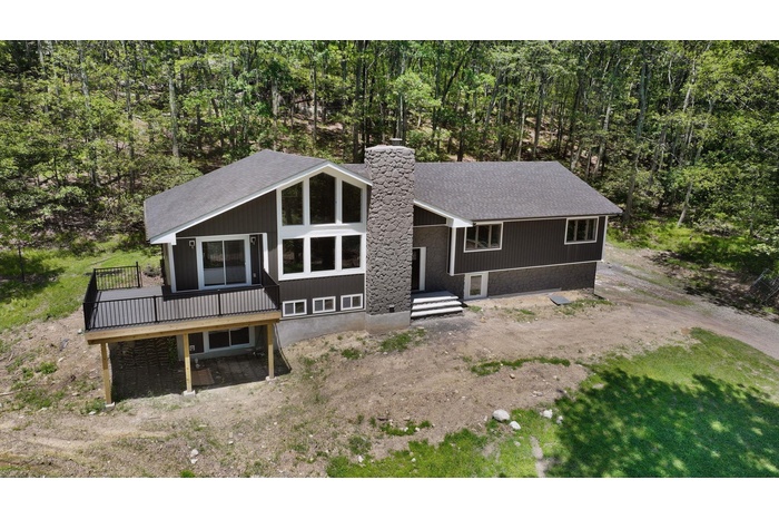 Back of property with a chimney, a deck, roof with shingles, and a view of trees
