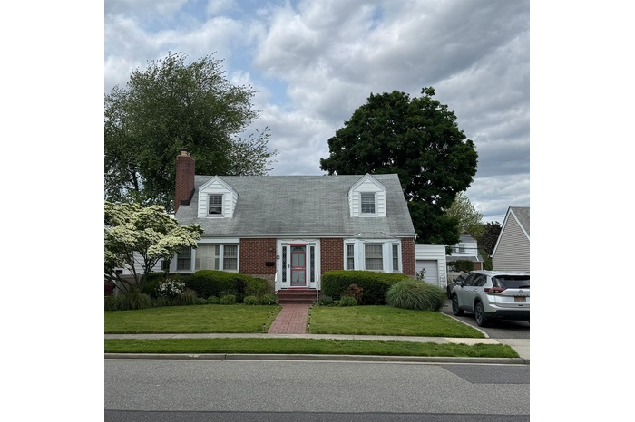 Cape cod home featuring brick siding, a front lawn, and a chimney