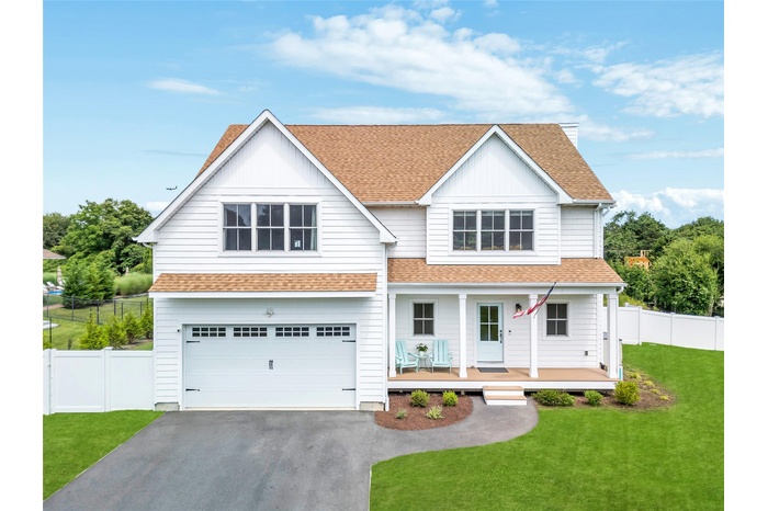 Traditional-style home featuring roof with shingles, driveway, an attached garage, covered porch, and board and batten siding