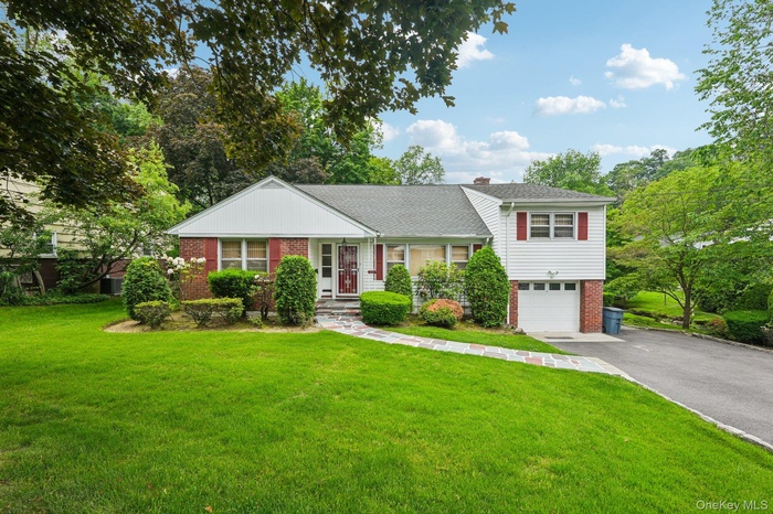 Split-level home featuring brick and vinyl siding, driveway, an attached garage, and a front lawn