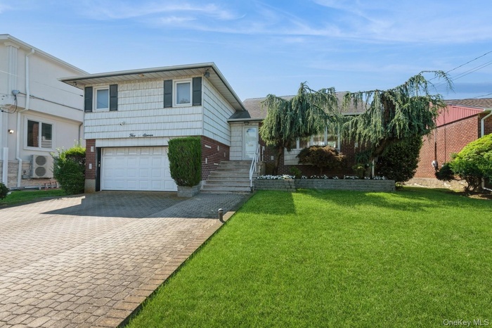 Split level home featuring brick siding, decorative driveway, a garage, and a front yard