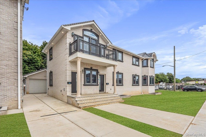 View of front of property featuring a front lawn, brick siding, a balcony, a garage, and french doors
