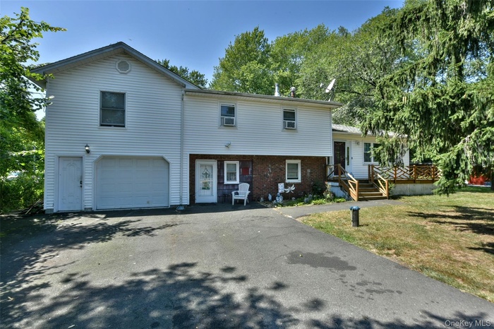 View of front facade featuring brick siding, asphalt driveway, a garage, a deck, and a front lawn