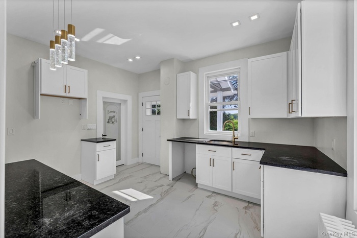Kitchen featuring light marble finish floors, hanging light fixtures, white cabinets, dark stone counters, and recessed lighting
