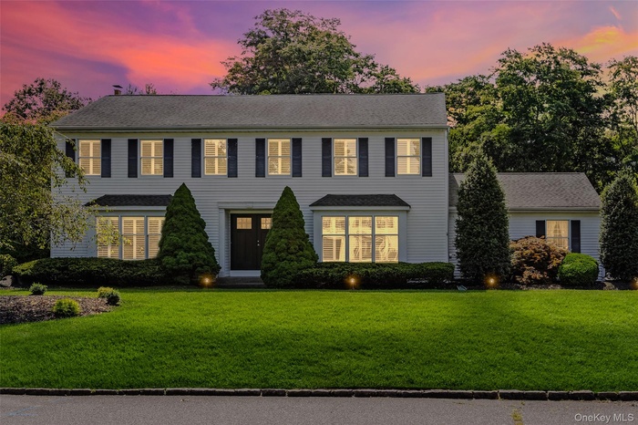 Colonial home featuring a front lawn and a shingled roof