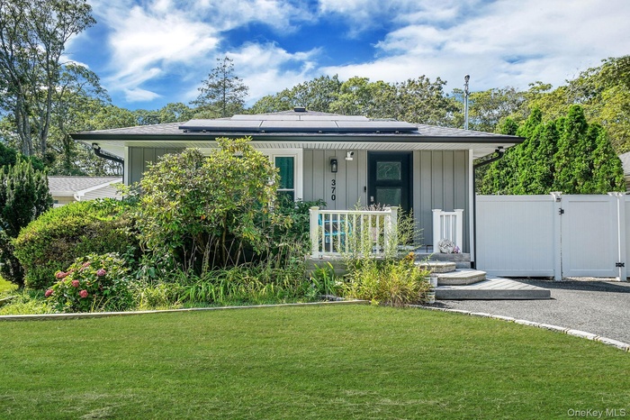View of front of home with roof mounted solar panels, a gate, a front yard, covered porch, and board and batten siding