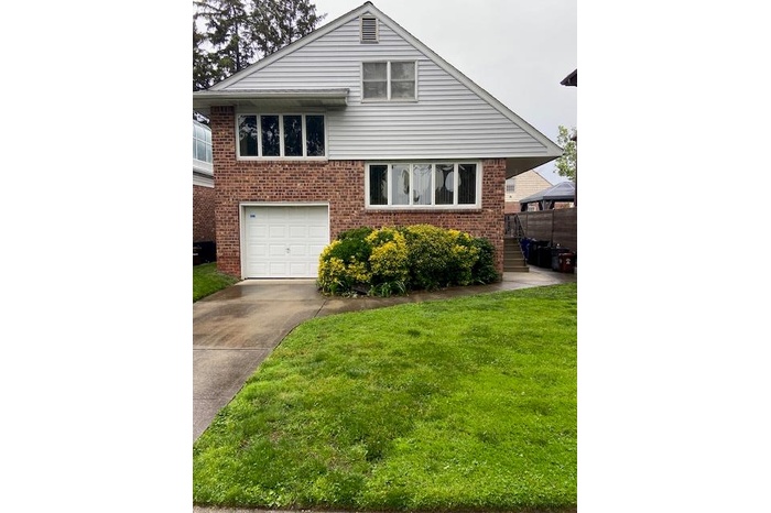 Split level home with brick siding, a garage, a front yard, and driveway