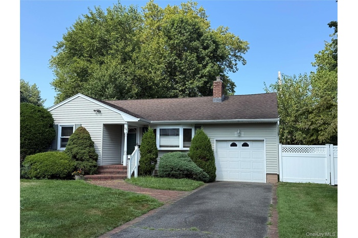 Ranch-style home featuring a garage, asphalt driveway, a chimney, and roof with shingles