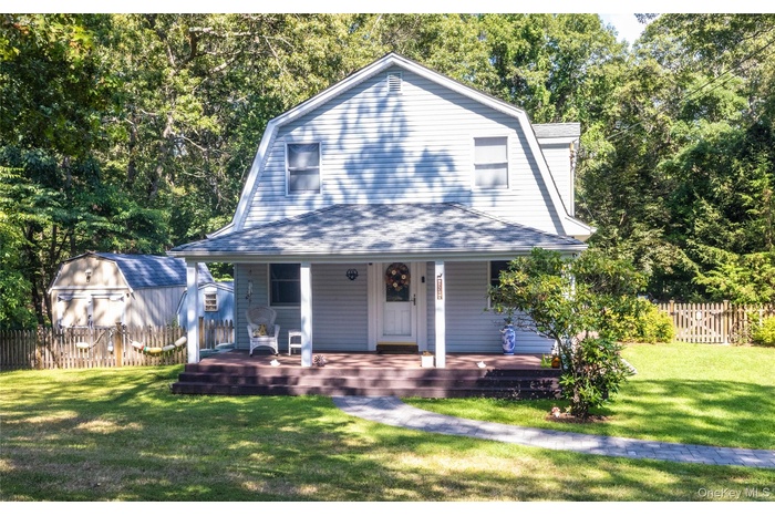Colonial inspired home featuring a gambrel roof, covered porch, a storage shed, and roof with shingles