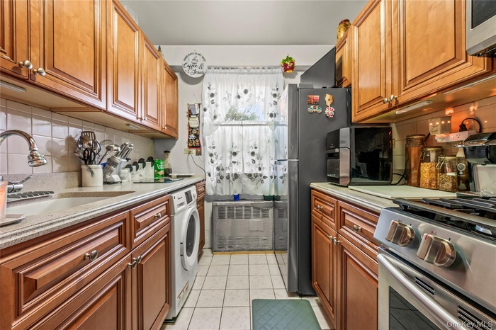 Kitchen featuring tasteful backsplash, stainless steel appliances, light tile patterned flooring, brown cabinetry, and washer / dryer