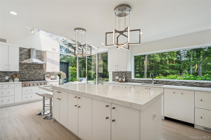 Kitchen featuring a sink, a kitchen island, decorative backsplash, wall chimney exhaust hood, and recessed lighting