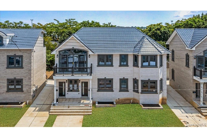 View of front of property featuring a balcony, brick siding, french doors, and a front lawn