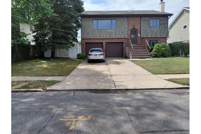 Raised ranch featuring brick siding, concrete driveway, a chimney, a front lawn, and a garage