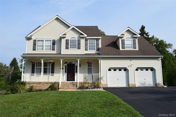 View of front of property with asphalt driveway, a porch, a shingled roof, a front yard, and stone siding