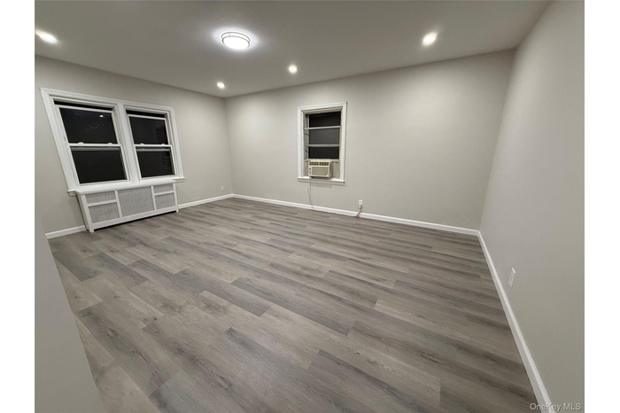 Empty room featuring wood finished floors, recessed lighting, and radiator heating unit
