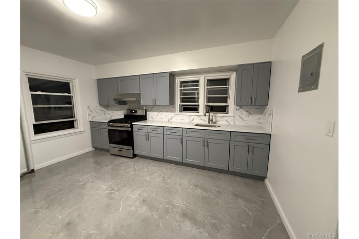 Kitchen with tasteful backsplash, gray cabinets, stainless steel gas range oven, electric panel, and light stone countertops