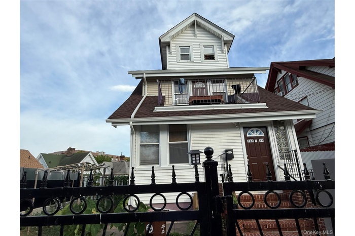 View of front of property featuring a fenced front yard, roof with shingles, a balcony, and a gate