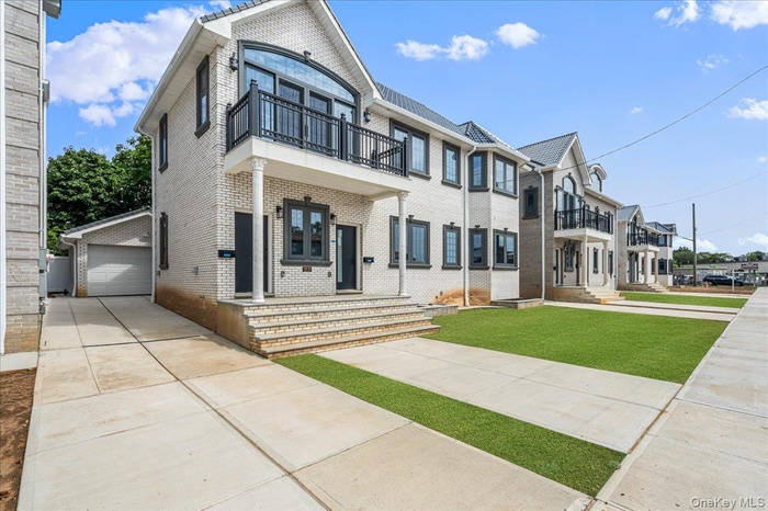 View of front of property featuring brick siding, a balcony, a detached garage, and a front yard