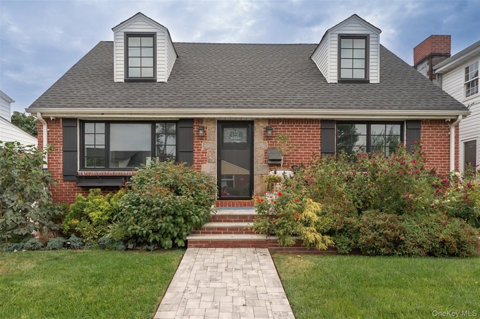 Cape cod-style house featuring brick siding, a front yard, and roof with shingles