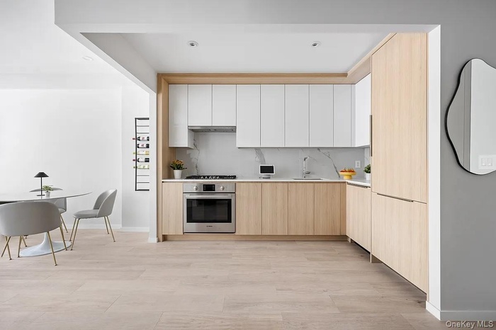 Kitchen with light brown cabinetry, stainless steel oven, modern cabinets, light countertops, and decorative backsplash