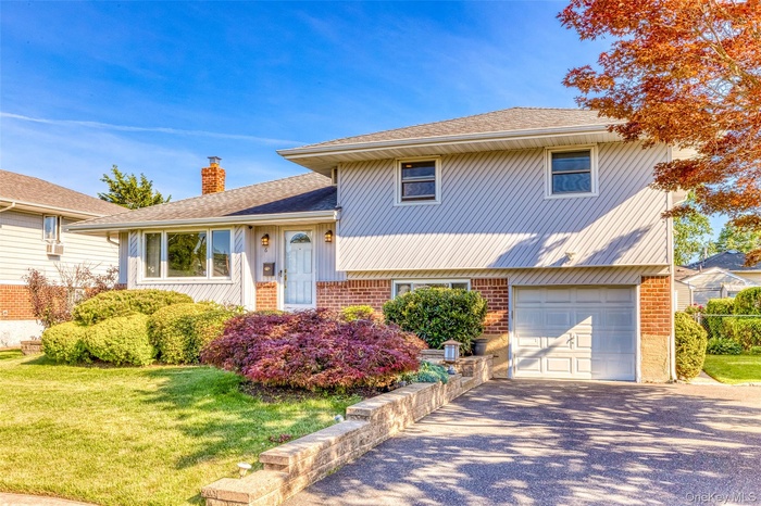 Split level home with a garage, brick siding, roof with shingles, driveway, and a chimney