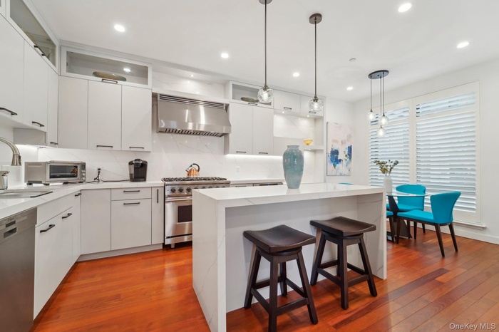 Kitchen featuring dark wood-style floors, a kitchen island, stainless steel appliances, and wall chimney range hood