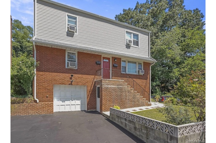 View of front facade with an attached garage, asphalt driveway, brick siding, and stairway