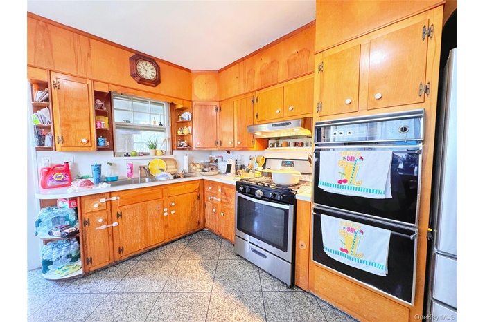 Kitchen featuring open shelves, appliances with stainless steel finishes, light countertops, brown cabinetry, and under cabinet range hood
