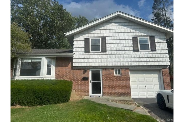 Back of property with a garage, brick siding, driveway, and a yard