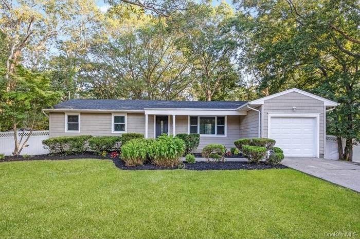 Ranch-style home featuring a garage, driveway, view of scattered trees, and a shingled roof