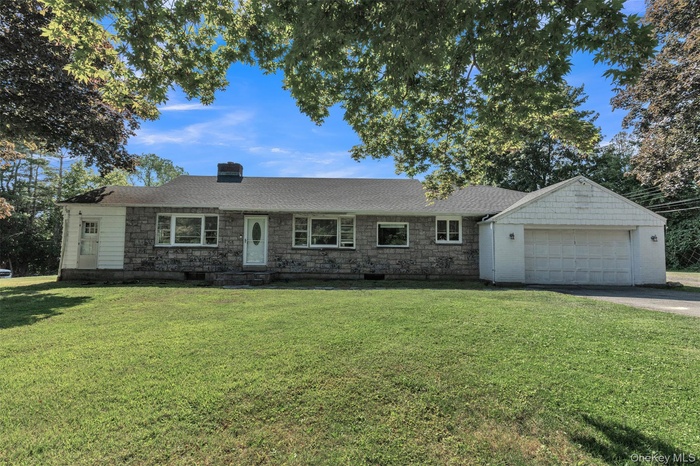 Single story home featuring a front yard, a chimney, a garage, and driveway
