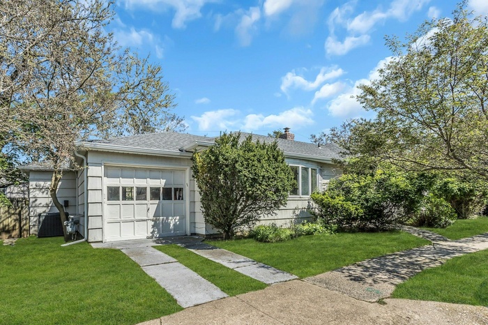 View of front of property featuring concrete driveway, a front yard, a chimney, and a shingled roof