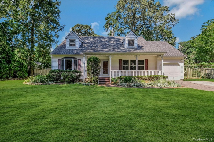 New england style home featuring a porch, a garage, a shingled roof, and driveway