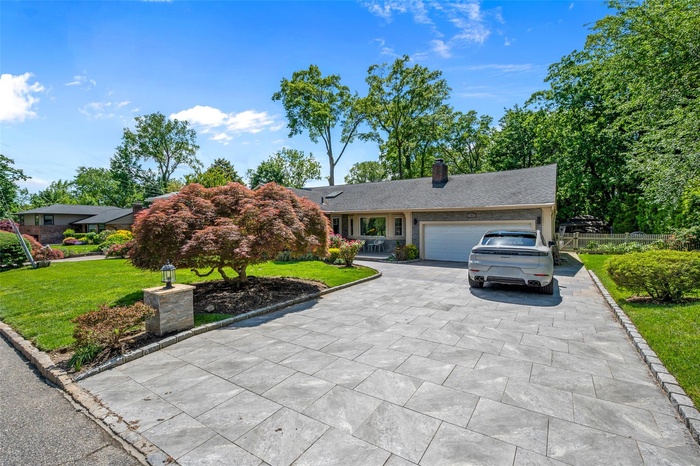 View of front facade with an attached garage, a chimney, and driveway