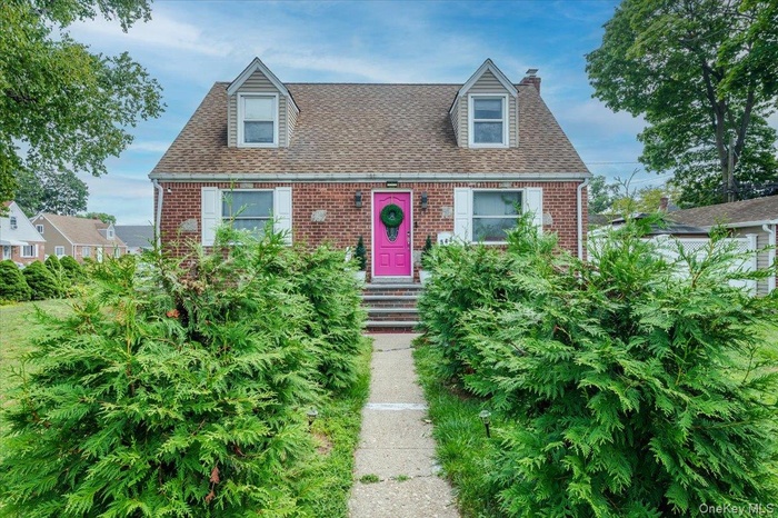 New england style home with brick siding, a shingled roof, and a chimney