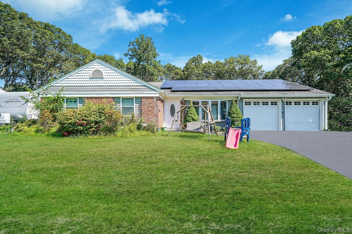 Ranch-style home with asphalt driveway, solar panels, a front yard, and a garage