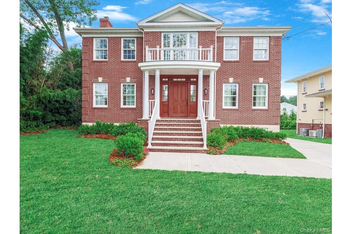 View of front of property featuring a front yard, brick siding, a chimney, and a balcony