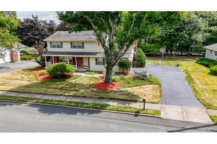 Traditional home featuring covered porch, brick siding, driveway, and a shingled roof