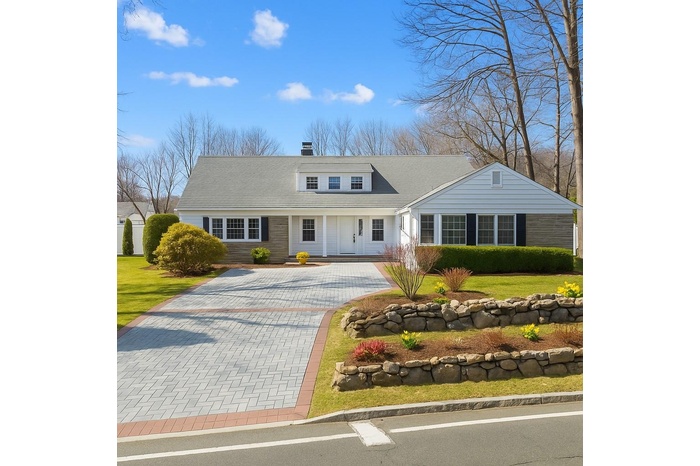 View of front of home featuring driveway, a chimney, and a front yard