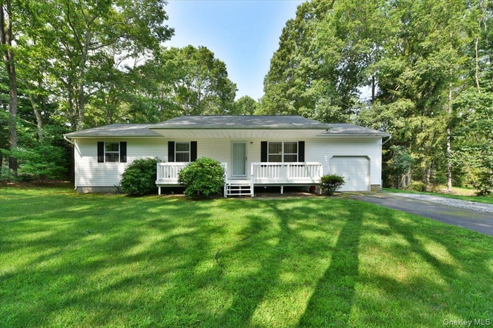 Ranch-style house with asphalt driveway, a garage, a porch, and a front yard