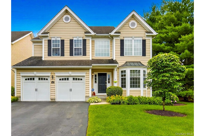 Traditional-style home with a garage, asphalt driveway, roof with shingles, and a front yard