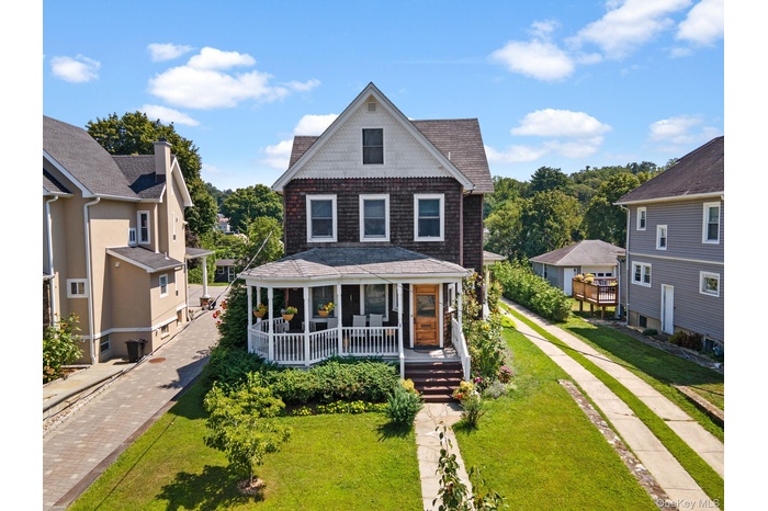 View of front facade with a front lawn, roof with shingles, and a porch