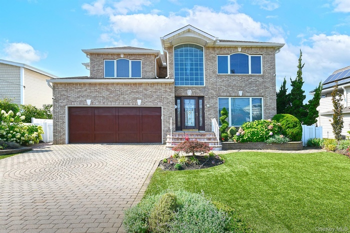 View of front of home with decorative driveway, a garage, a front yard, and brick siding