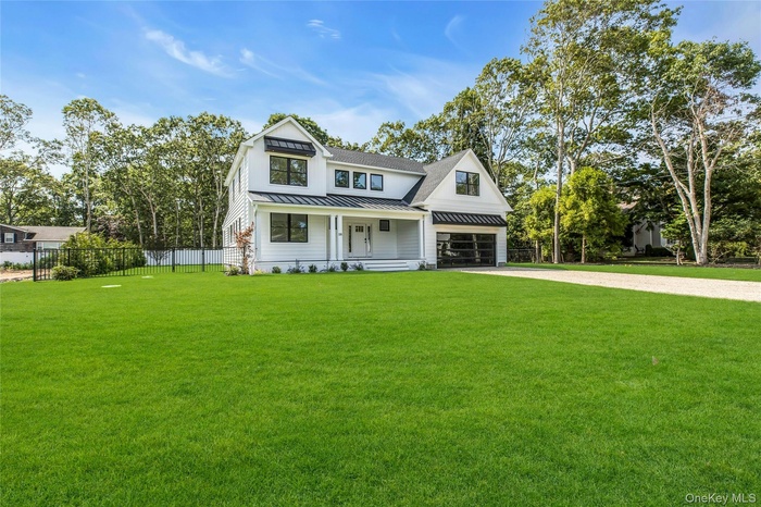 Modern inspired farmhouse with a standing seam roof, a metal roof, covered porch, driveway, and view of scattered trees
