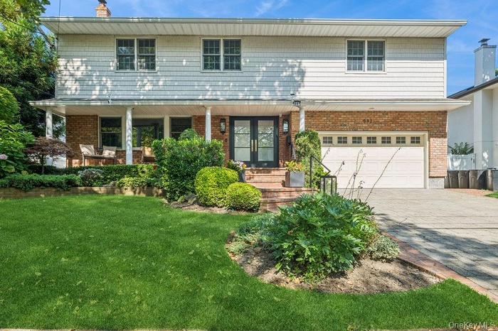 Traditional-style home with an attached garage, driveway, a porch, and brick siding
