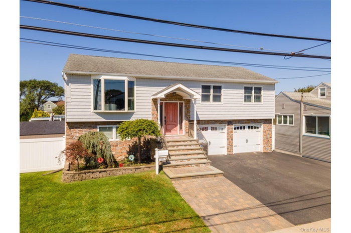Bi-level home featuring stone siding, a garage, asphalt driveway, a shingled roof, and a front lawn