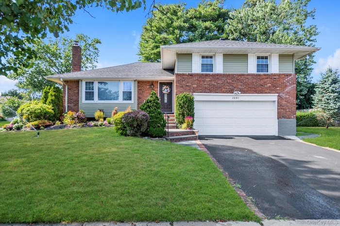 Split level home featuring an attached garage, asphalt driveway, a front yard, and a chimney